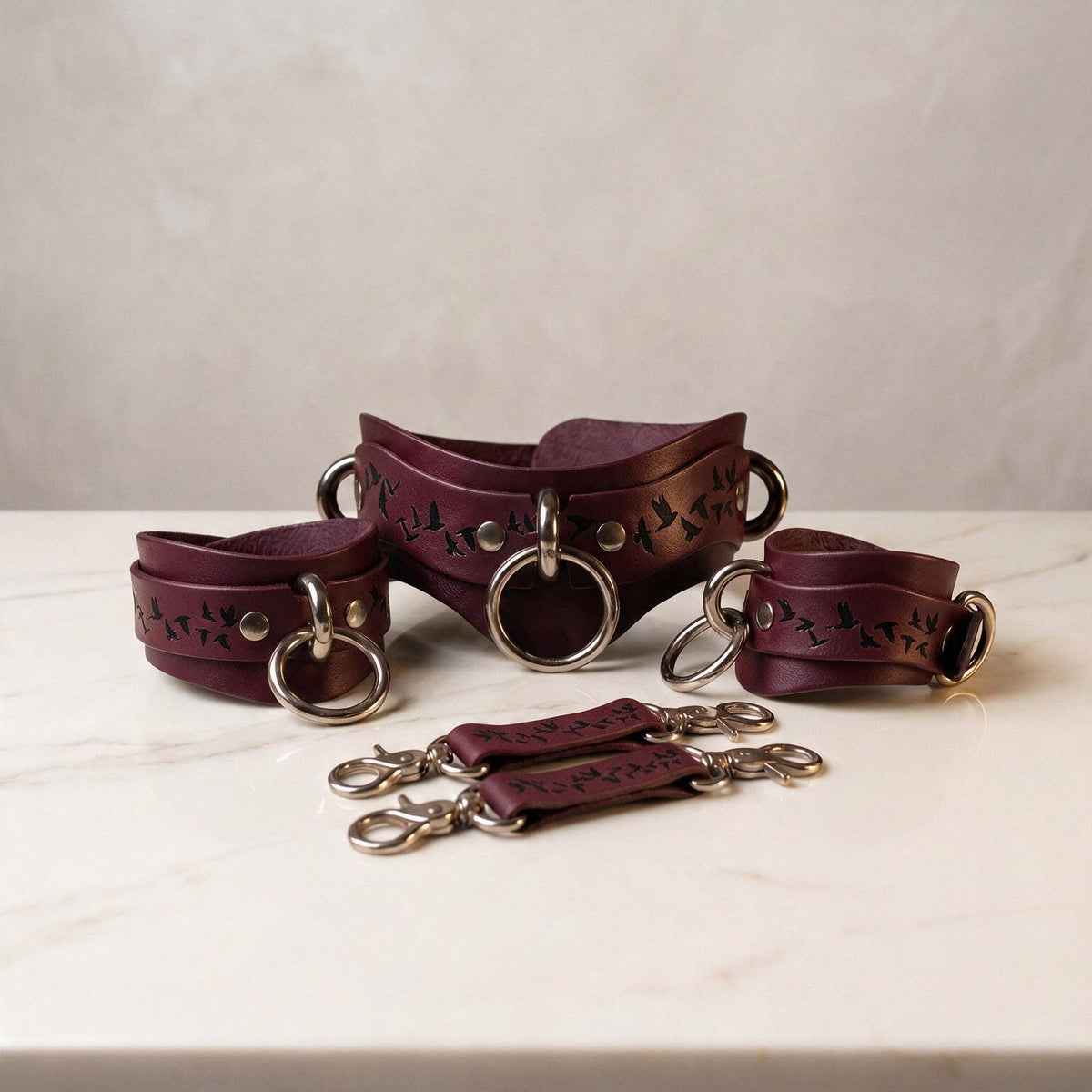 a collection of burgundy leather straps with metal rings and buckles, arranged on a white marble surface.
