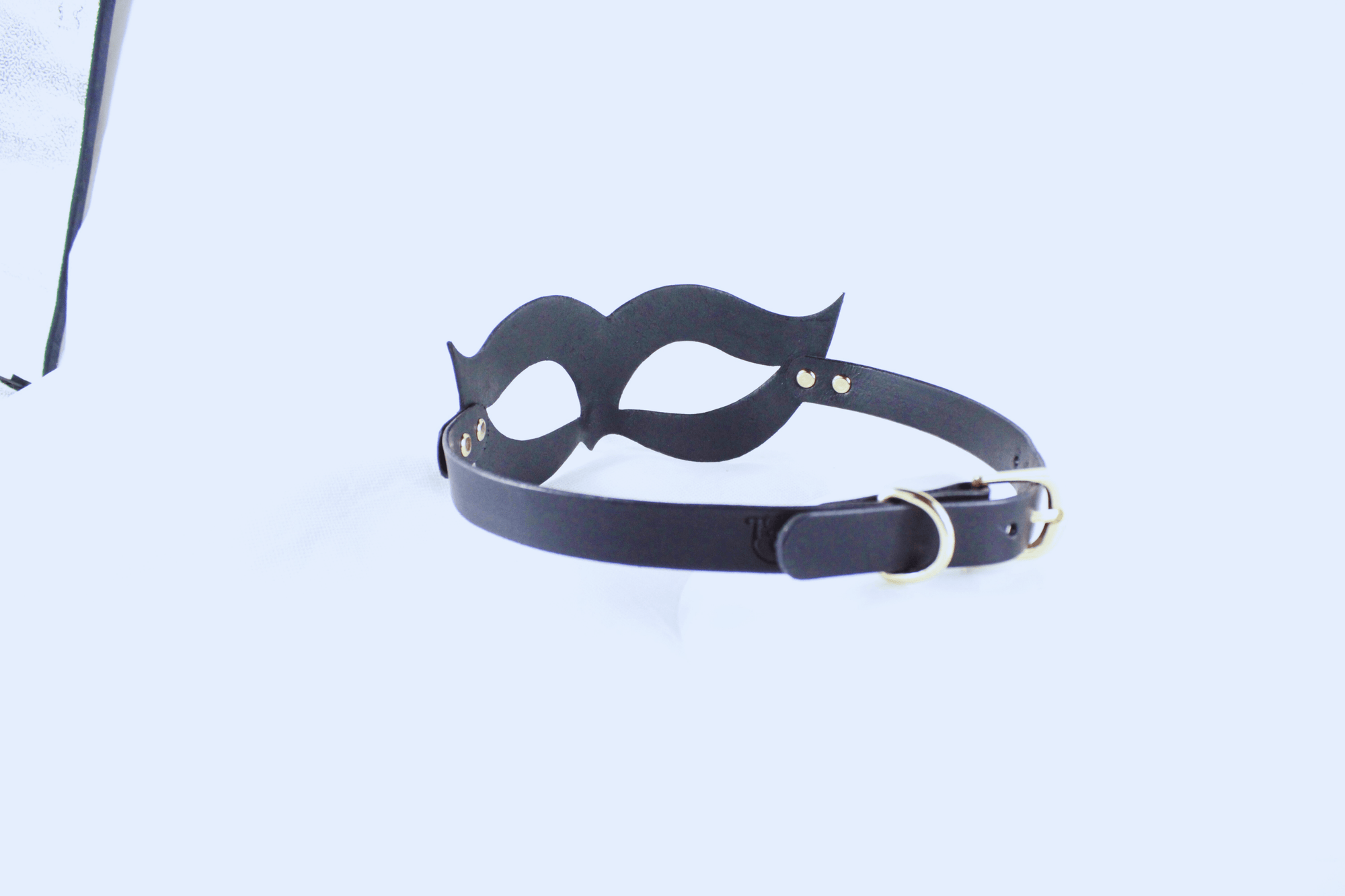 A black mask with a black strap and a gold buckle is shown against a white background.
