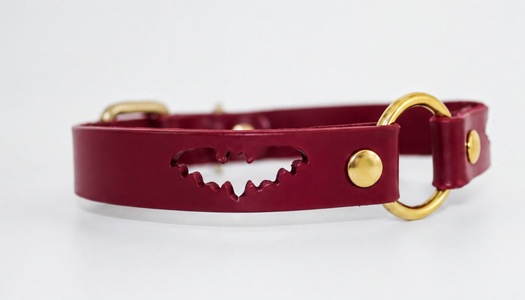 A burgundy leather collar with a bat cutout design and two gold-colored buckles.