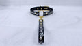A black collar with a gold-colored buckle and a floral pattern on the strap is displayed against a white background.