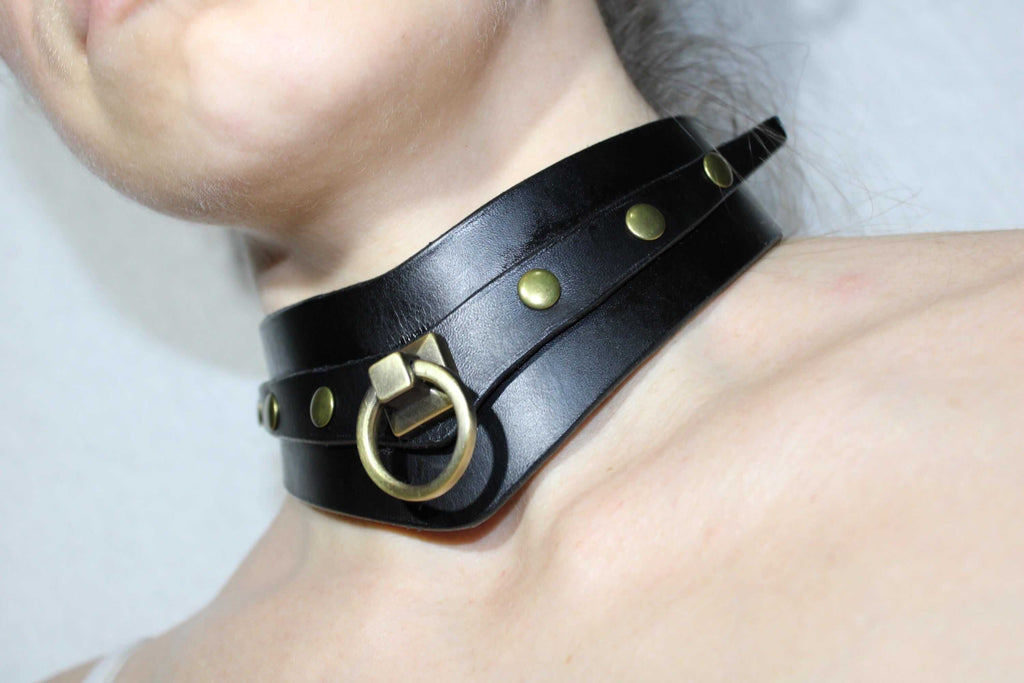 A close-up view of a person's neck wearing a black leather choker necklace with gold-colored studs and a metal ring.