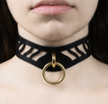 A close-up of a person's neck and chest area, featuring a black choker necklace with a gold ring and a cutout design.