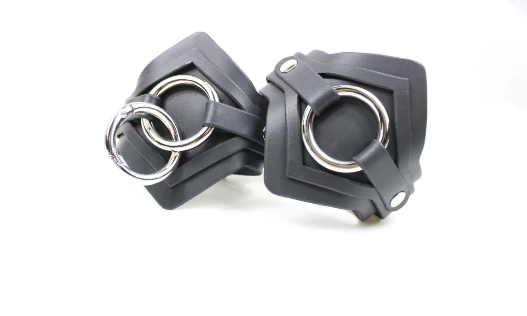 A pair of black leather straps with metal rings and buckles, arranged side by side.