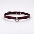 A burgundy leather choker collar with a metal ring and buckle.