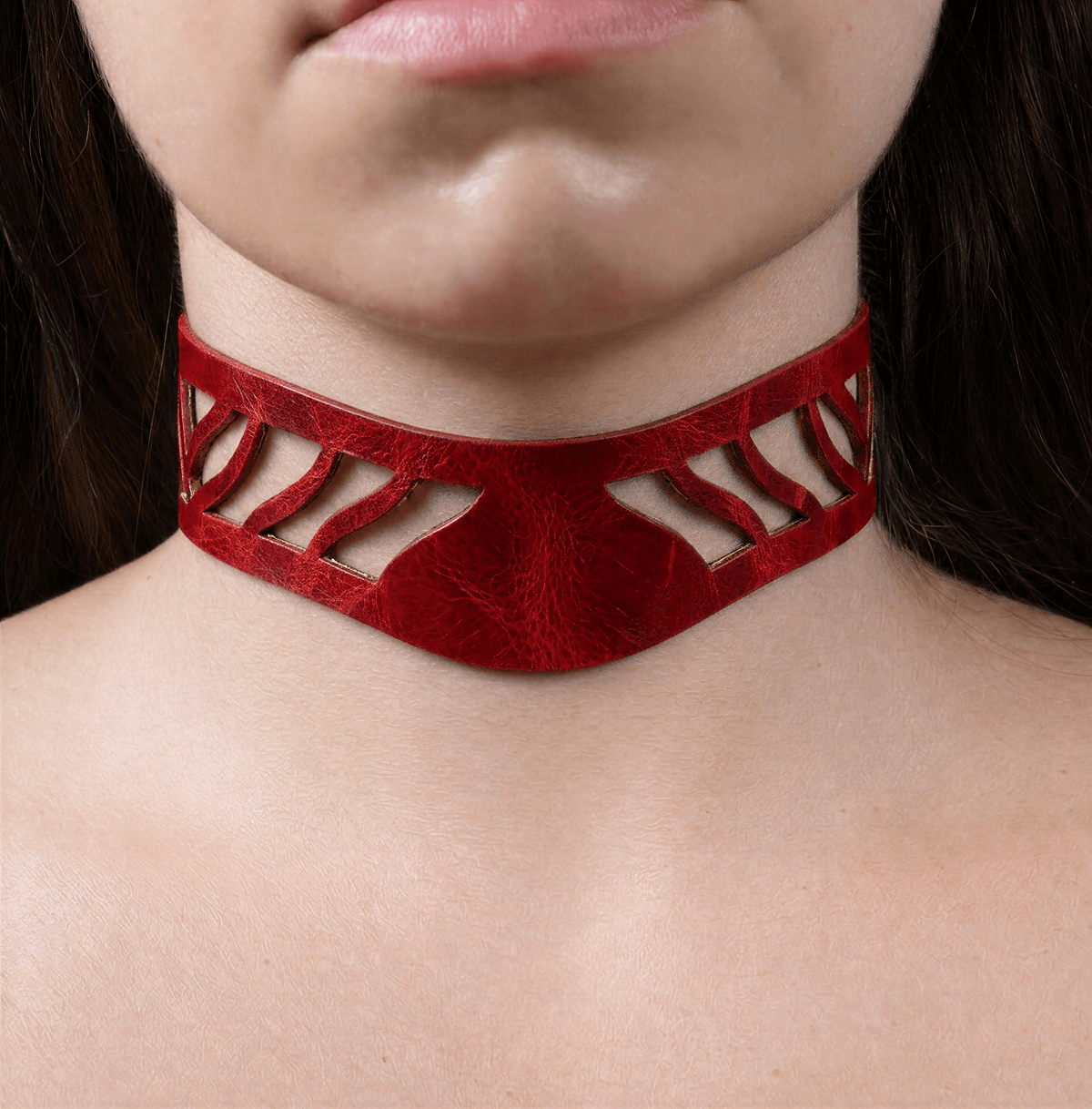 A close-up of a person's neck and chest area wearing a red choker necklace with a unique cutout design.
