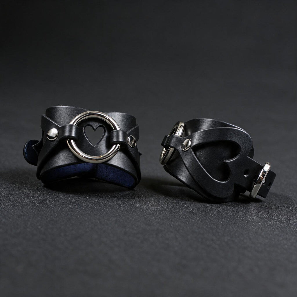 two black leather cuffs with heart-shaped holes, placed on a dark surface.