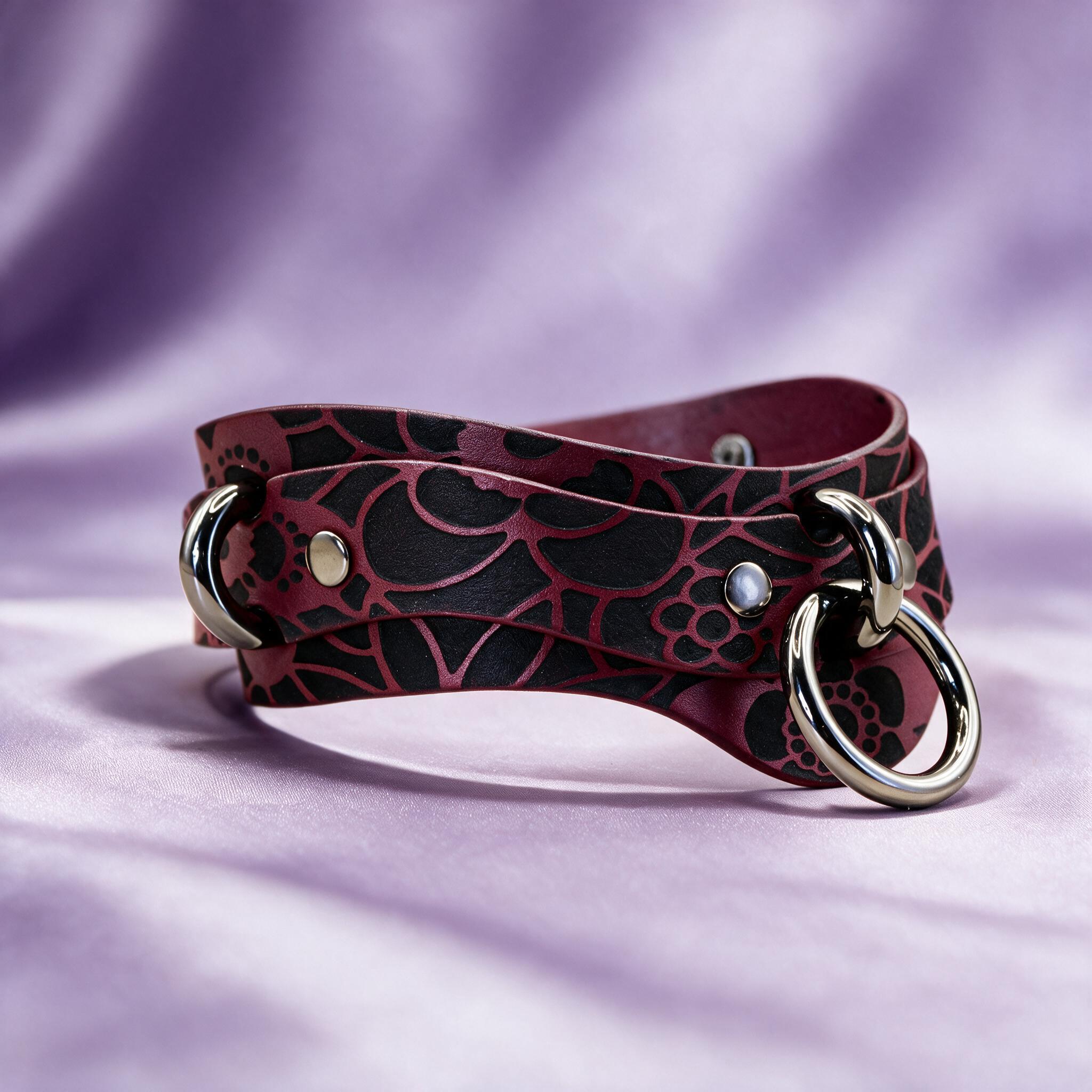 A burgundy leather choker necklace with a floral pattern and metal rings is displayed against a purple background.