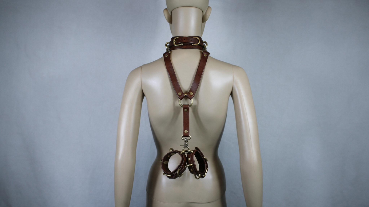 A mannequin wearing a leather strap with multiple buckles and a chain around its neck.