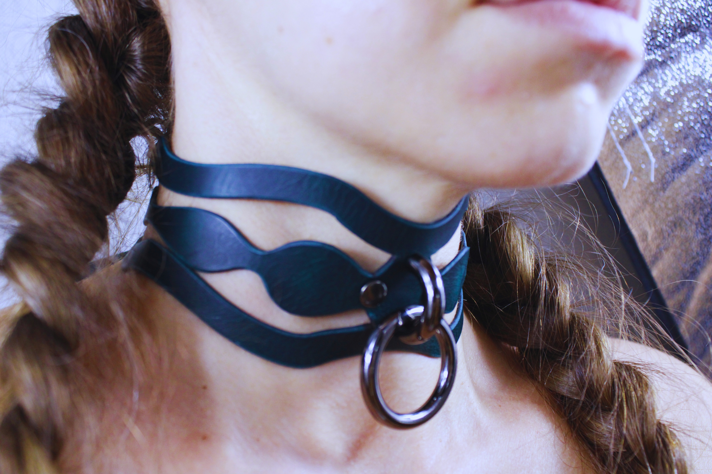A close-up of a person's neck wearing a dark blue leather choker necklace with a metal ring.
