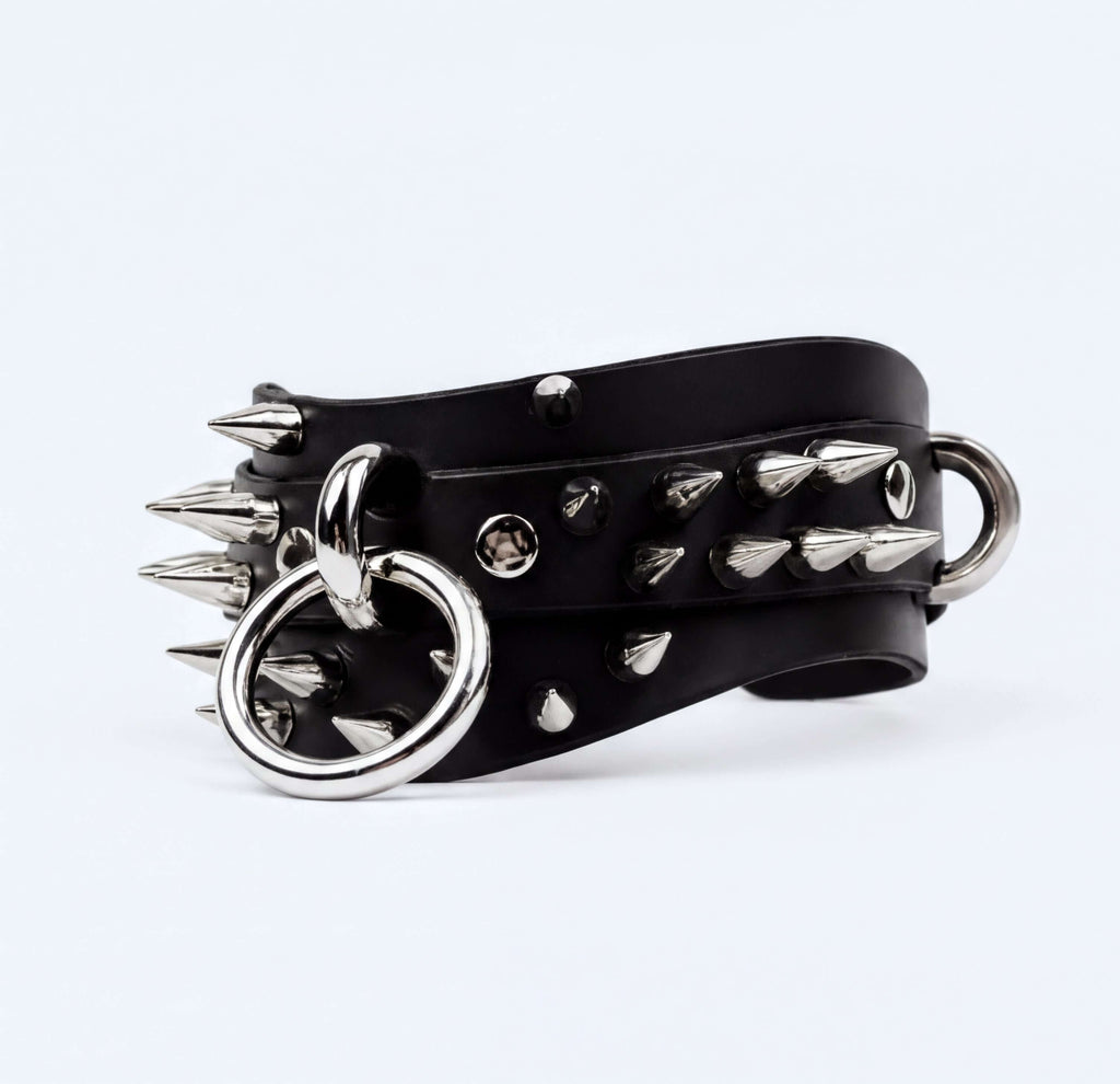 A black leather bracelet with silver spikes and rings, creating a bold and edgy appearance.