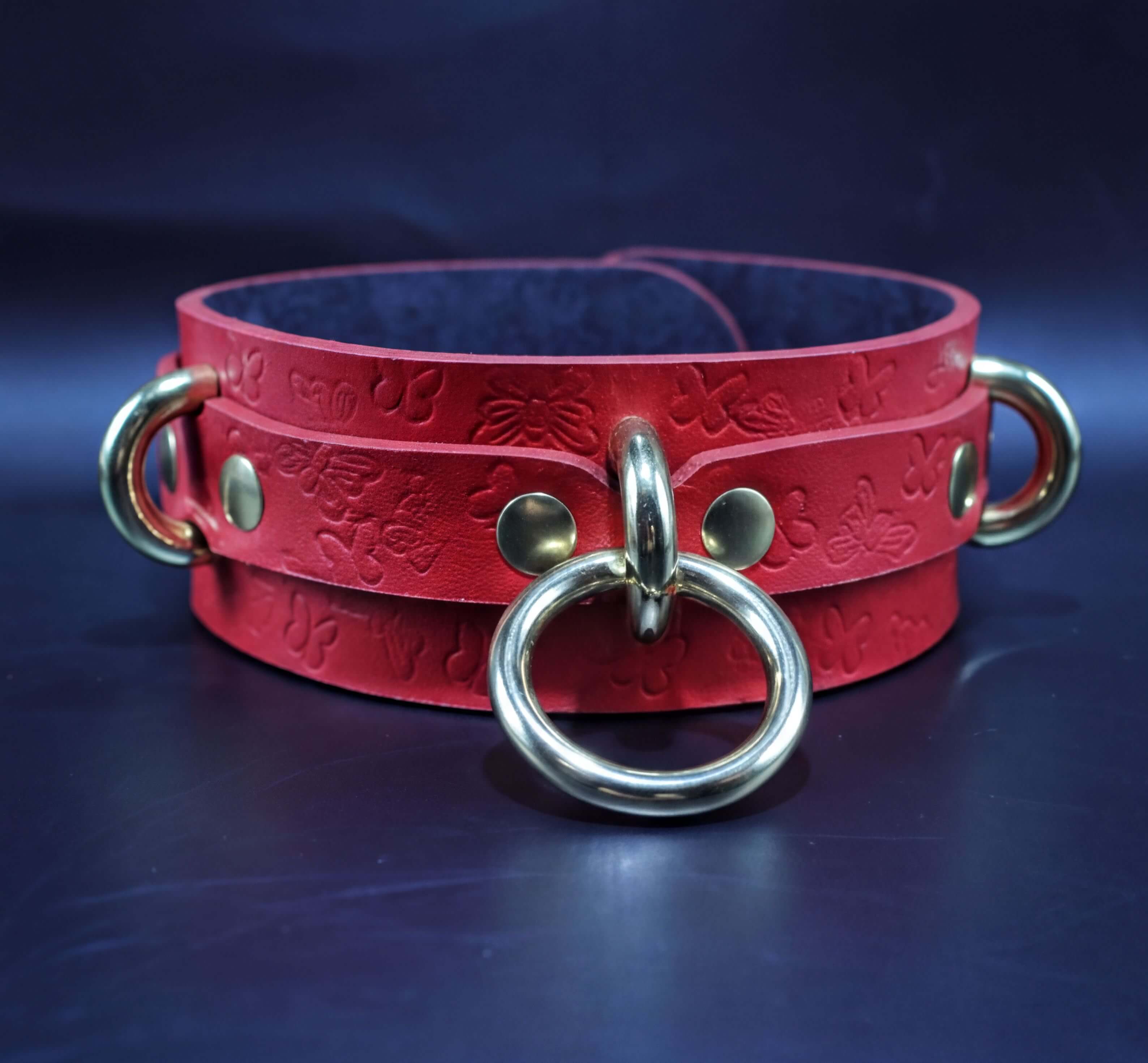 A red leather choker collar with gold metal rings and a black interior.