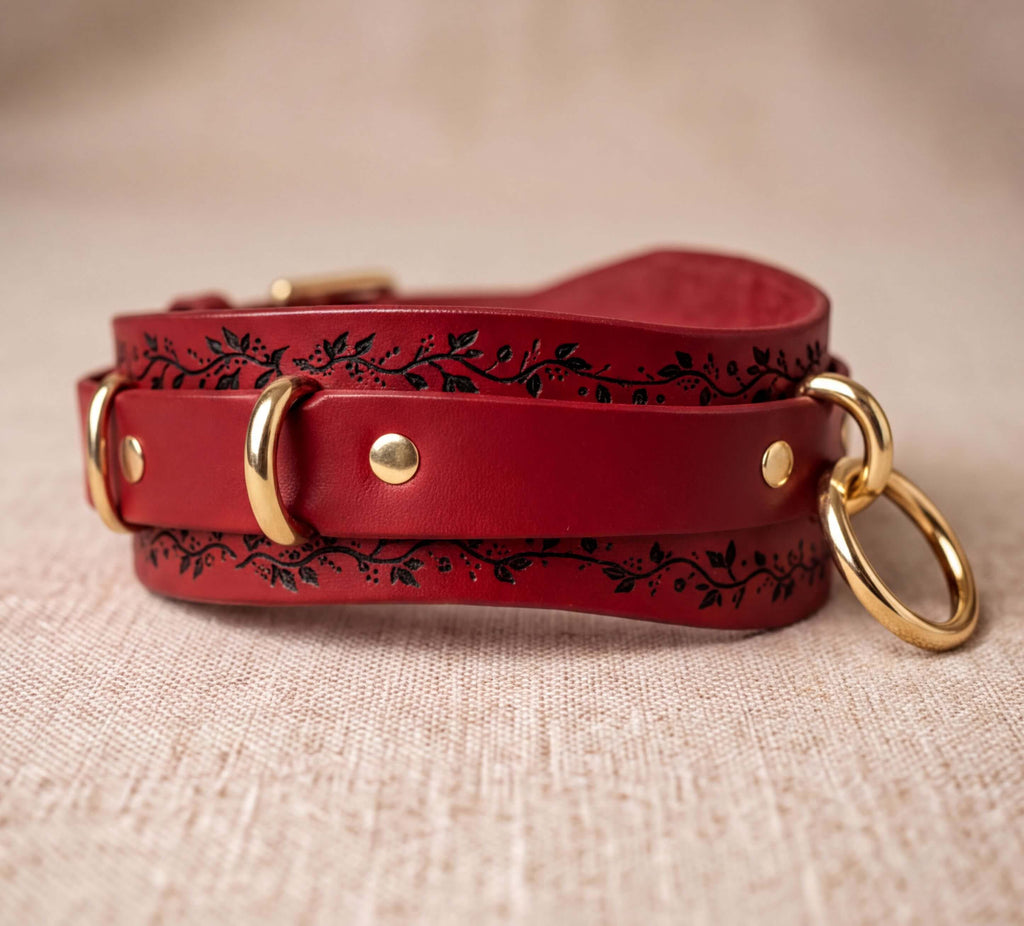 A red leather strap with a decorative pattern and two gold rings on the ends, resting on a beige surface.