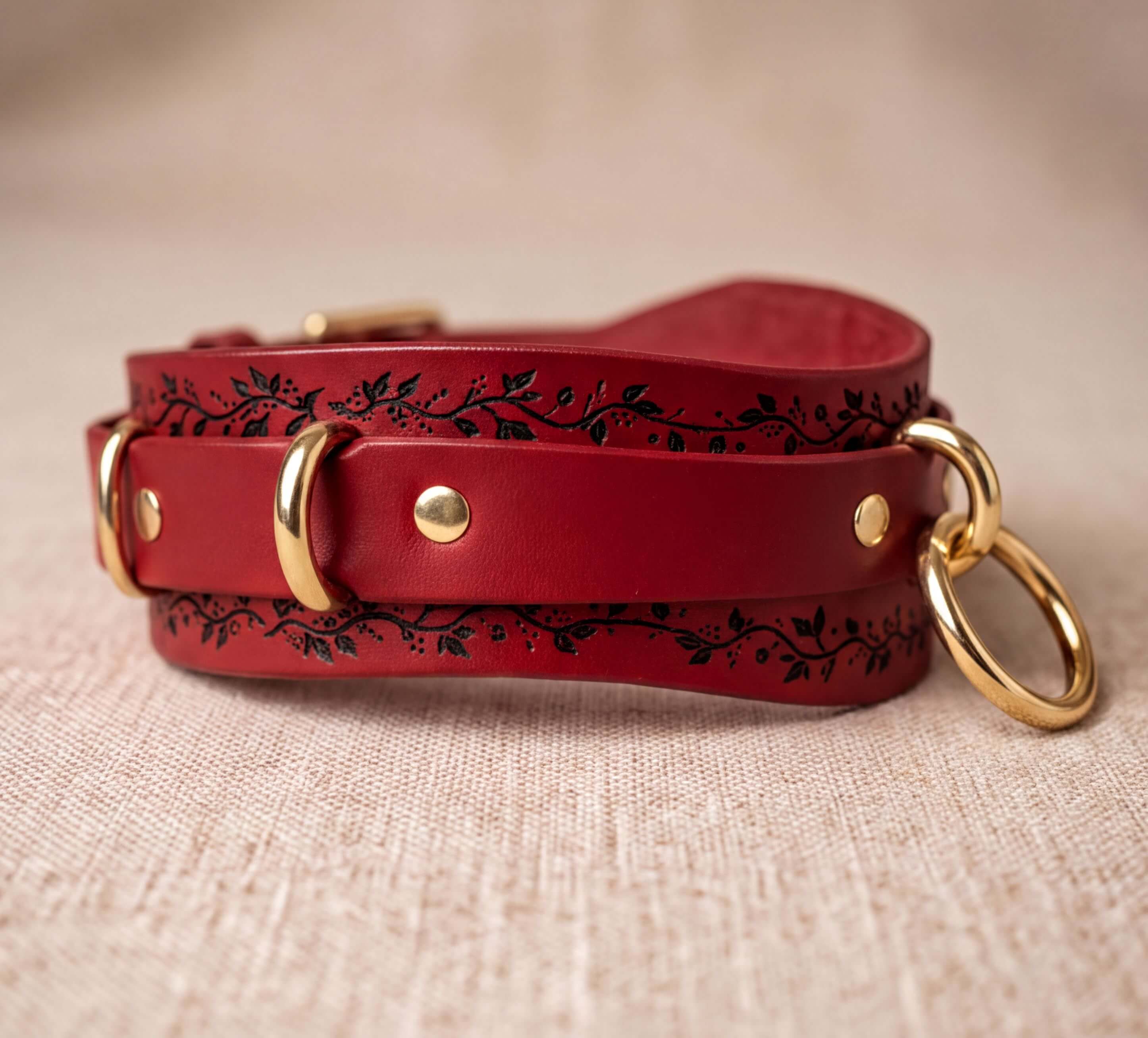 A red leather strap with a decorative pattern and two gold rings on the ends, resting on a beige surface.