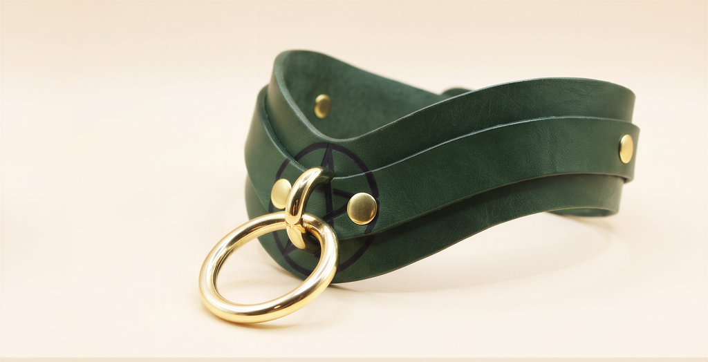 A green leather choker necklace with a gold ring and two gold-colored buckles.