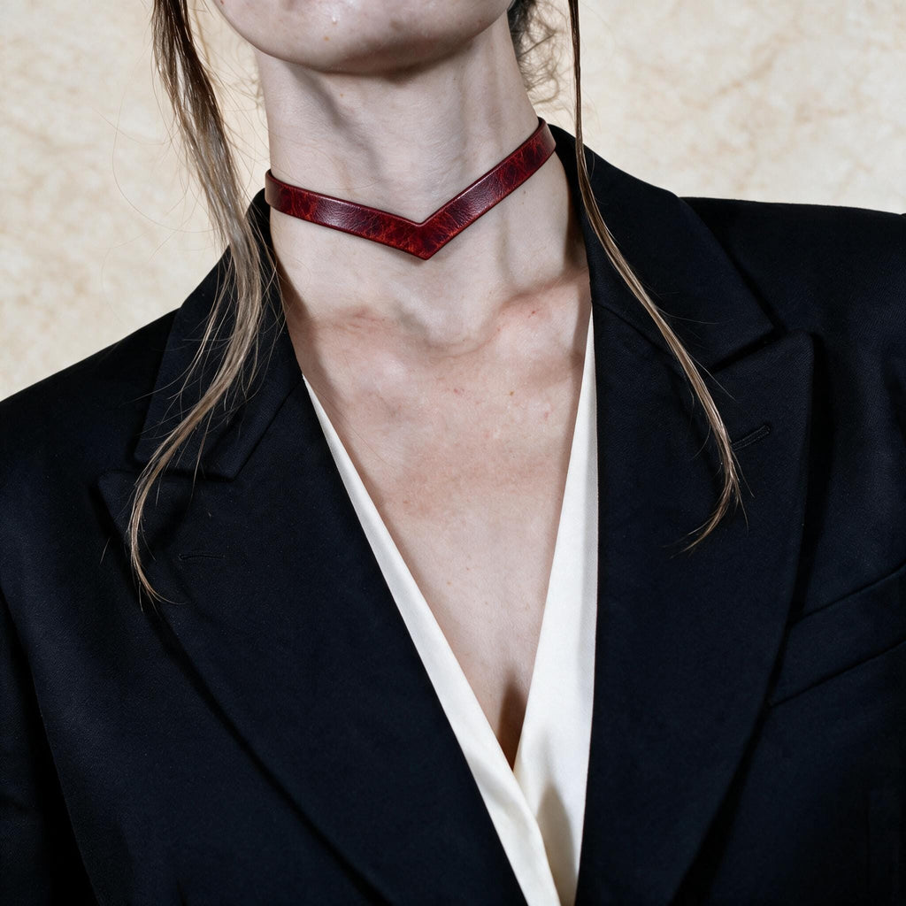A close-up of a person wearing a black blazer and a red choker necklace.