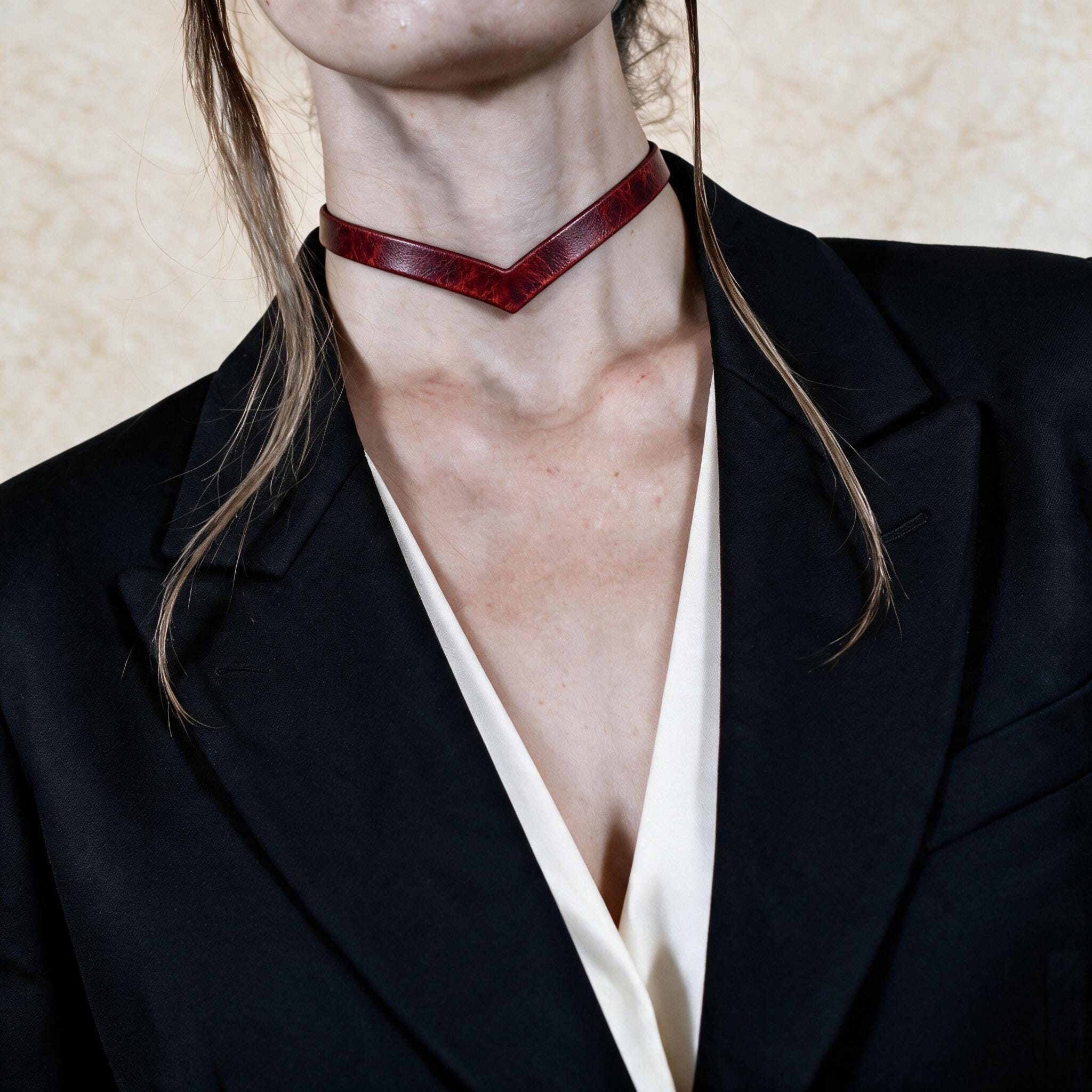 A close-up of a person wearing a black blazer and a red choker necklace.