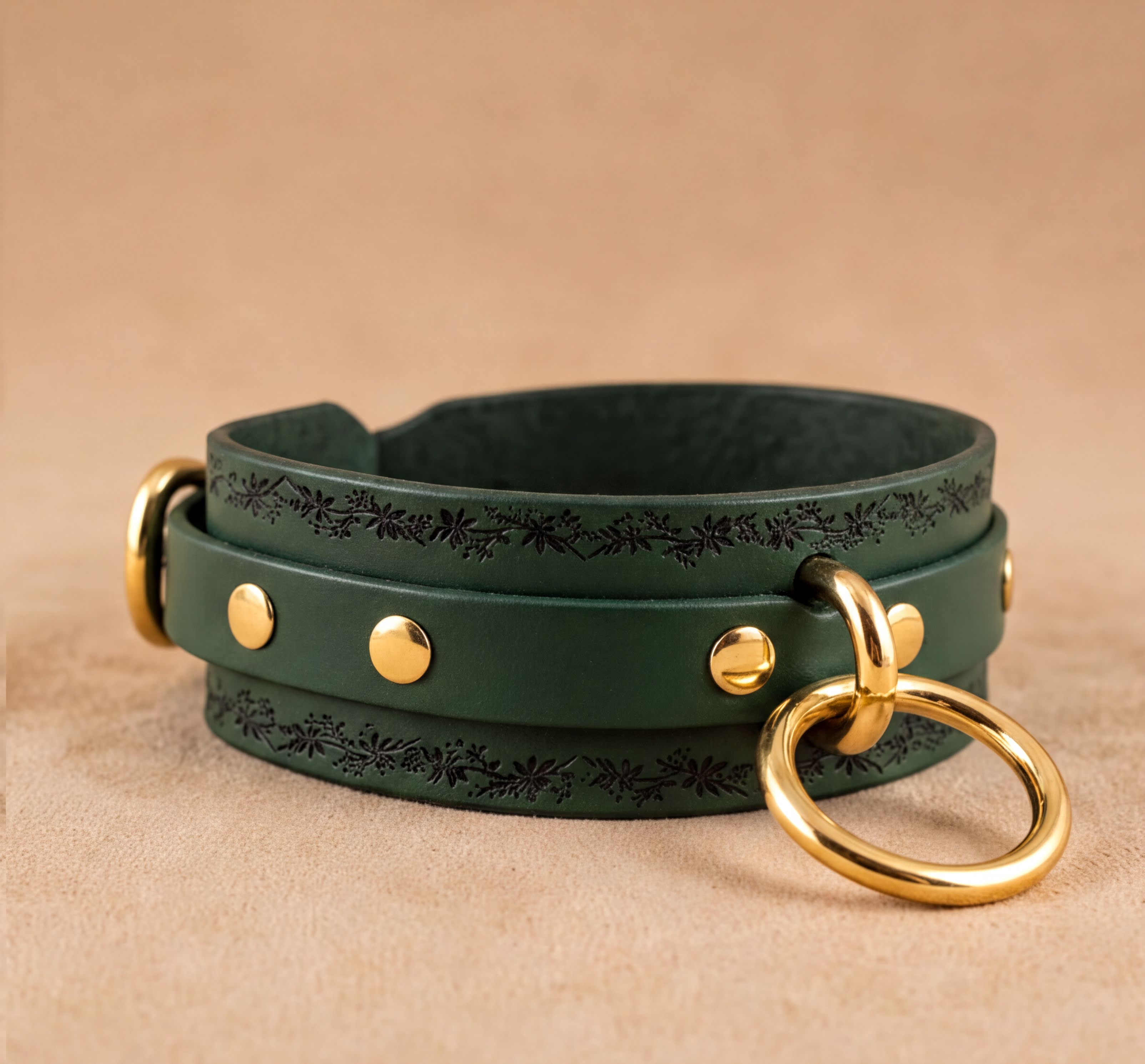 A green leather choker necklace with gold metal rings and a decorative leaf pattern on the front.