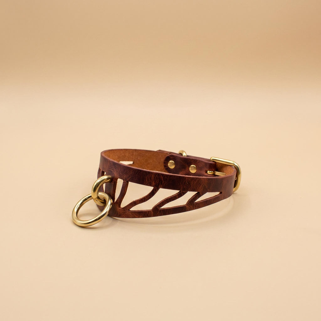 A brown leather choker necklace with a cutout design and two gold-colored rings.