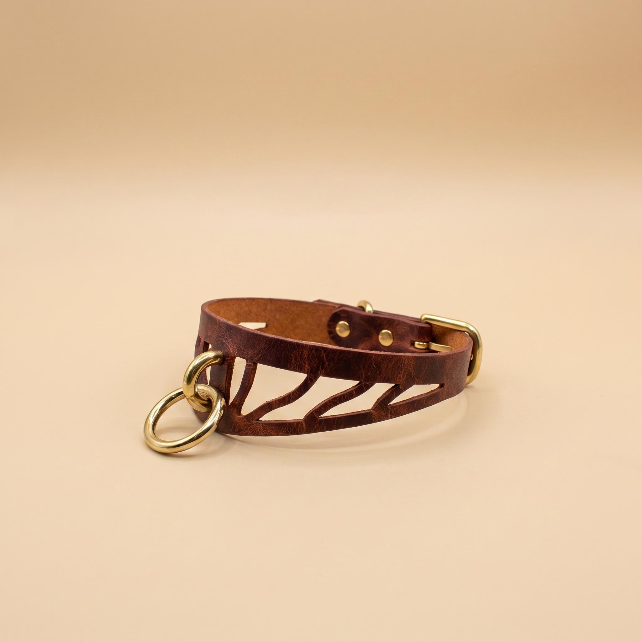 A brown leather choker necklace with a cutout design and two gold-colored rings.
