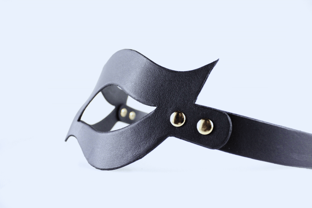 A black leather mask with a curved shape and two gold-colored buckles.