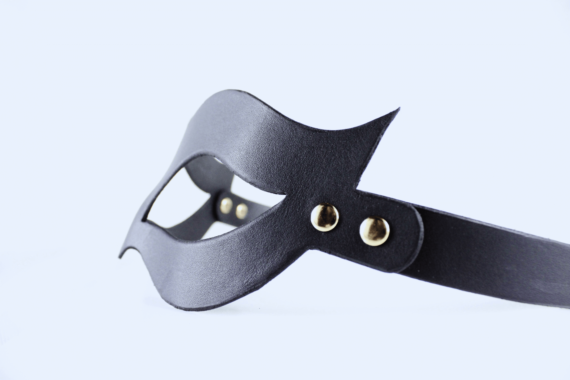 A black leather mask with a curved shape and two gold-colored buckles.