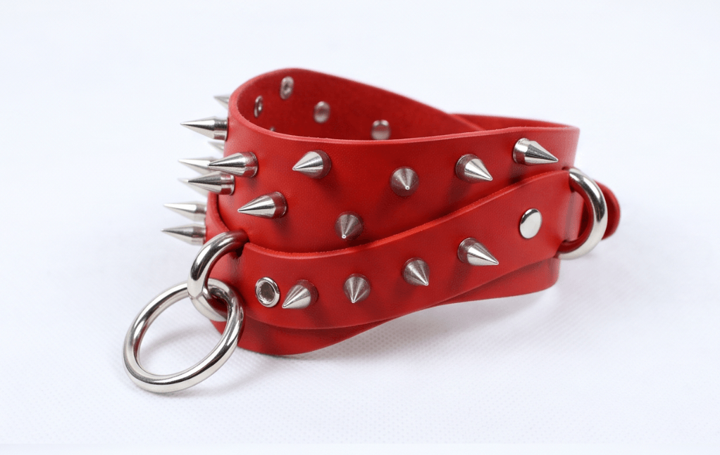 A red leather strap with silver spikes protruding from it, attached to a metal ring.