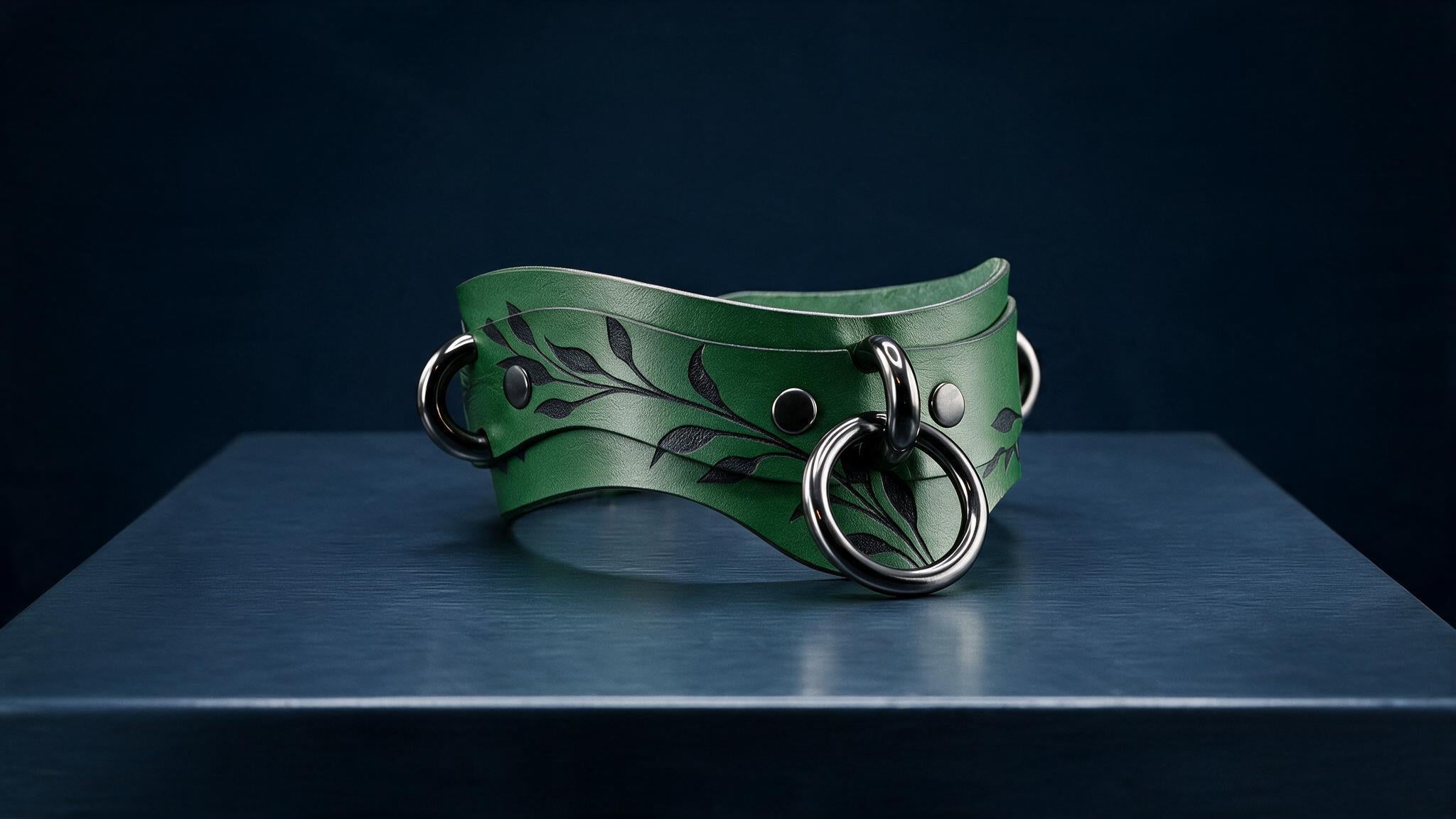 A green leather choker necklace with a leaf design and metal rings is displayed on a dark surface.