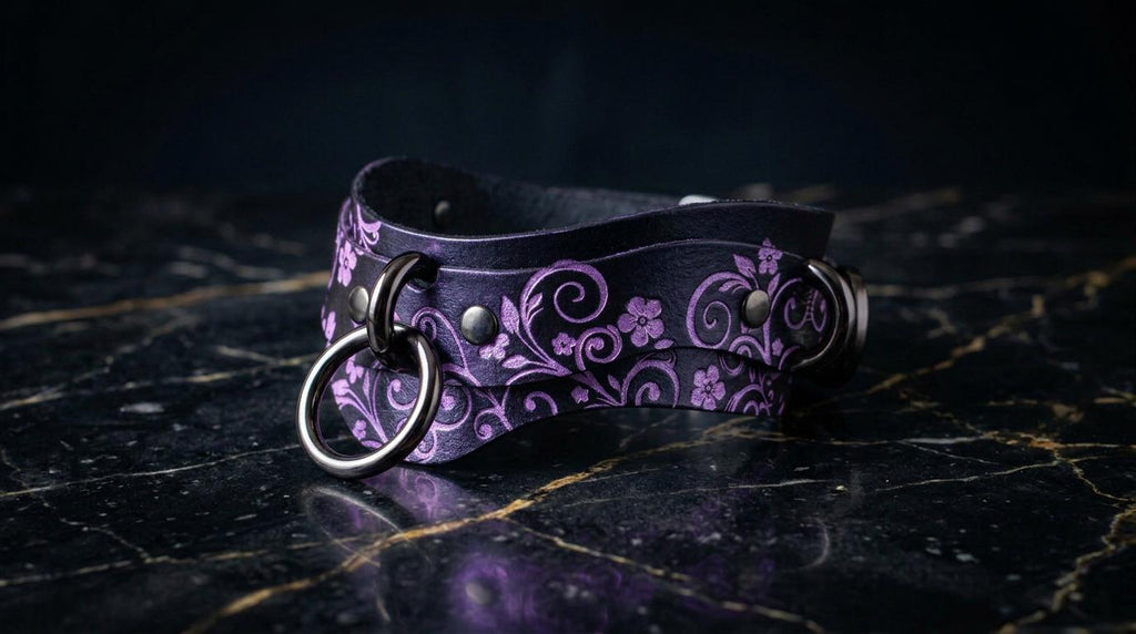 A purple leather choker necklace with a floral pattern and metal rings is displayed on a dark marble surface.