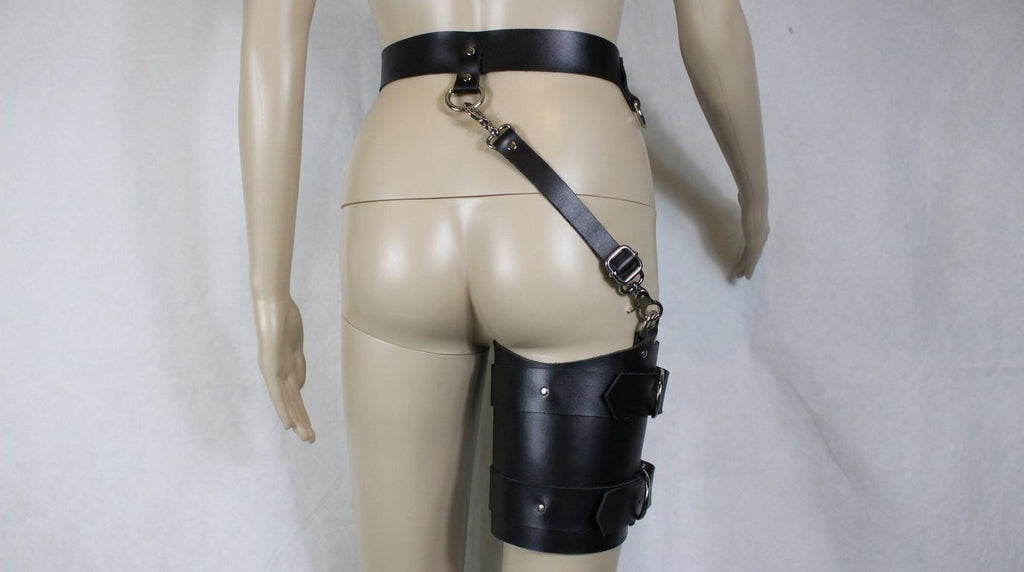 A mannequin wearing a black leather thigh-high garter belt with a leather strap and metal clasp.