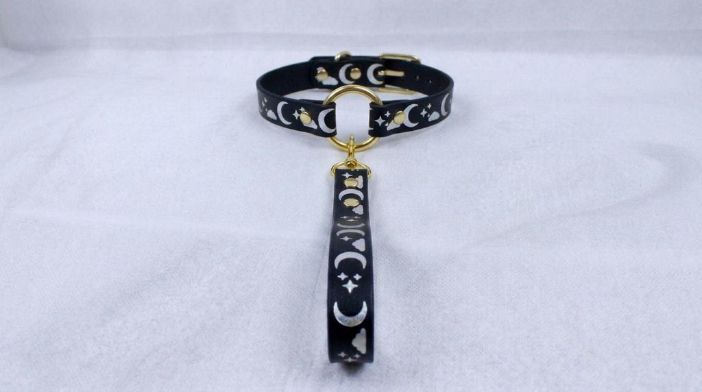 A black collar with a gold-colored metal clasp and a dangling charm featuring a moon and star design.