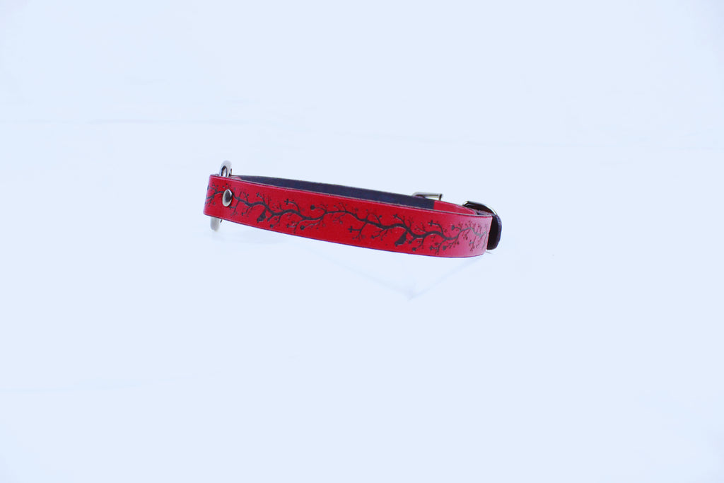 A red dog collar with a black design on it is shown against a white background.