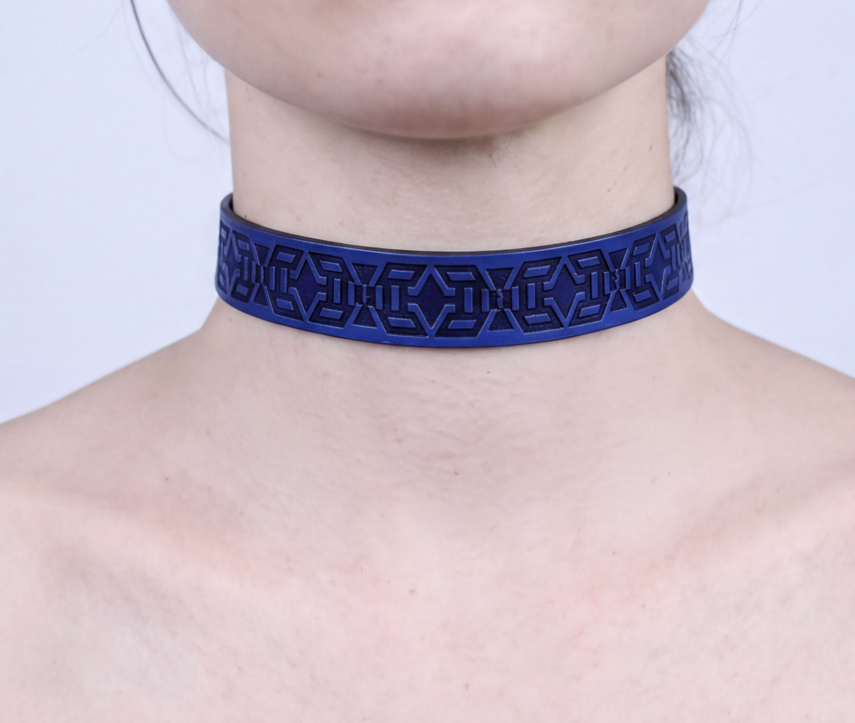 A close-up view of a person's neck and chest area wearing a blue choker necklace with a geometric pattern.