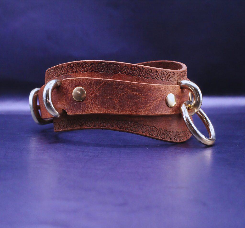 A brown leather strap with metal rings and a decorative pattern on it, resting on a blue surface.