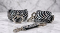 a pair of zebra-striped leather straps with metal rings and buckles, arranged on a marble surface.