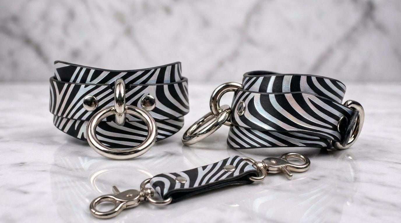 a pair of zebra-striped leather straps with metal rings and buckles, arranged on a marble surface.