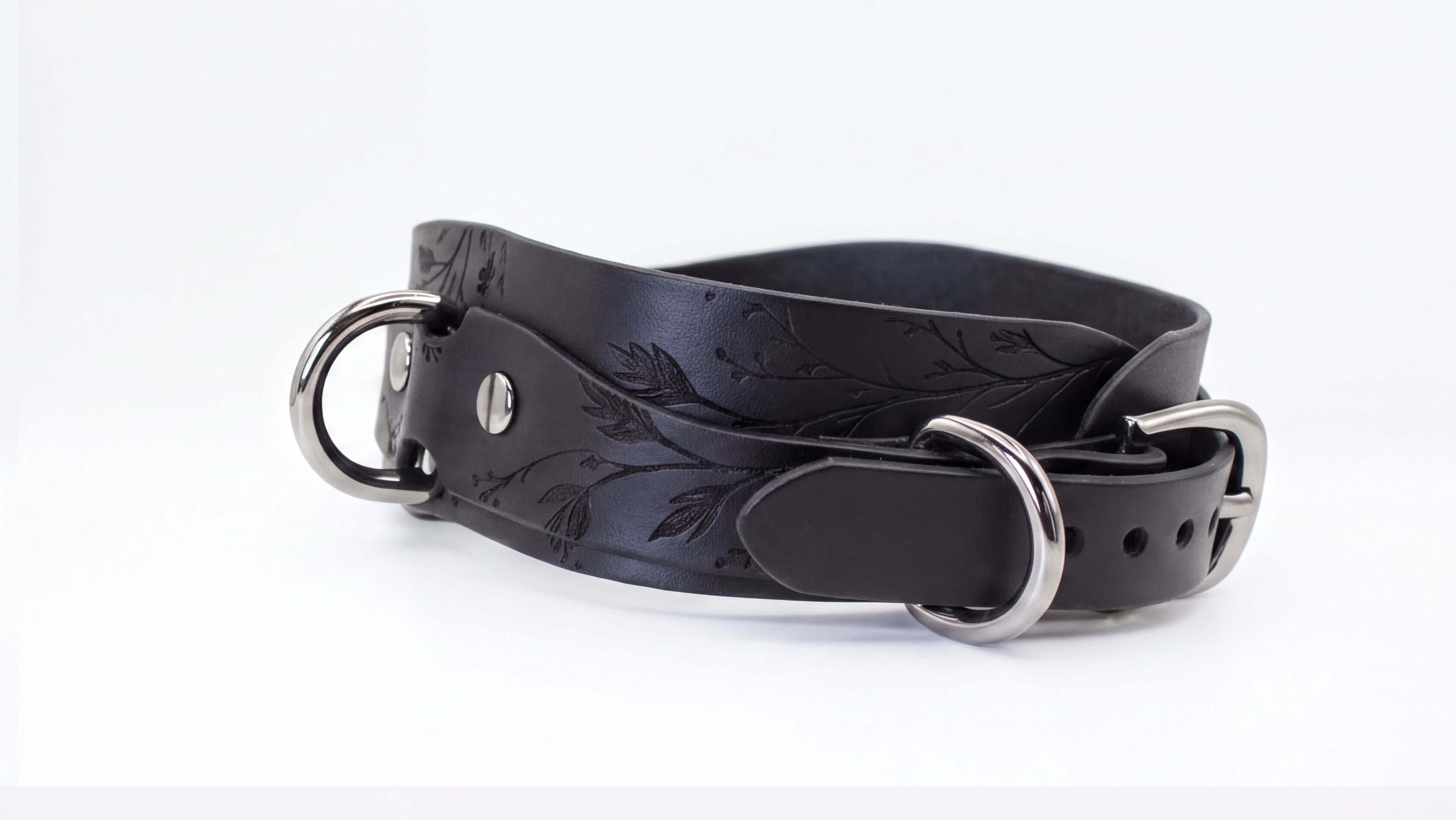 A black leather belt with metal buckles and a floral pattern on the surface.