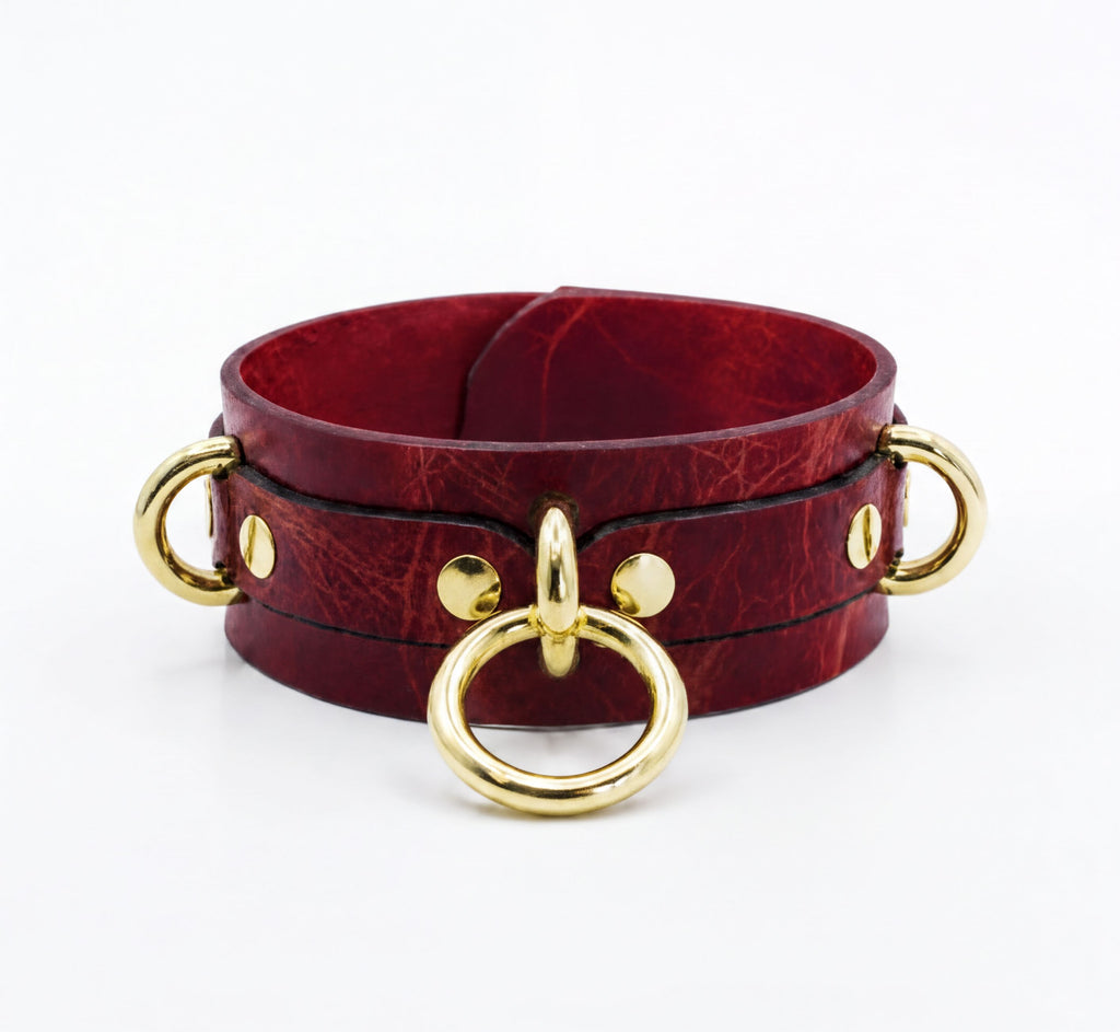 A burgundy leather choker necklace with gold metal rings and buckles.