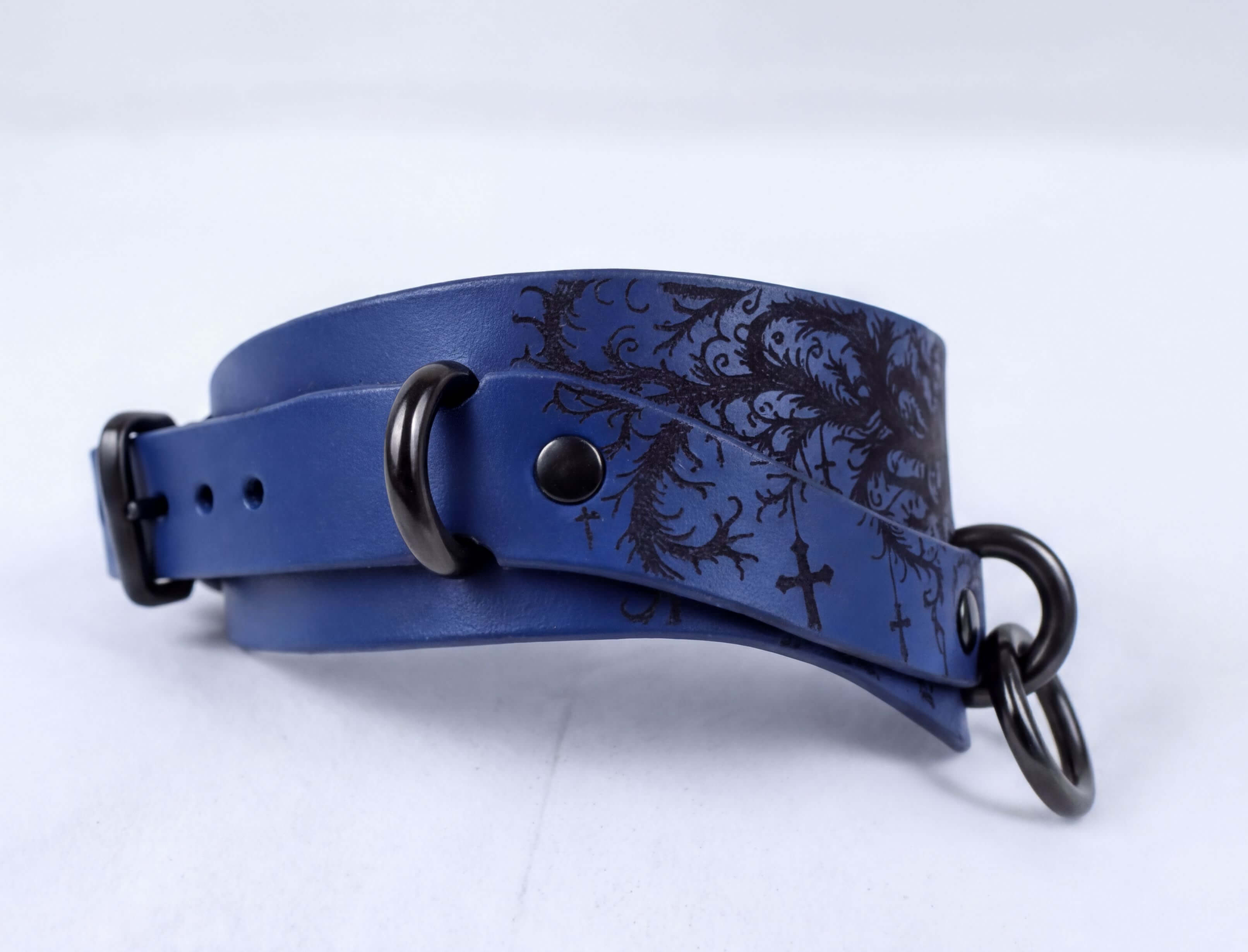 A blue leather choker necklace with a black floral design and metal rings.