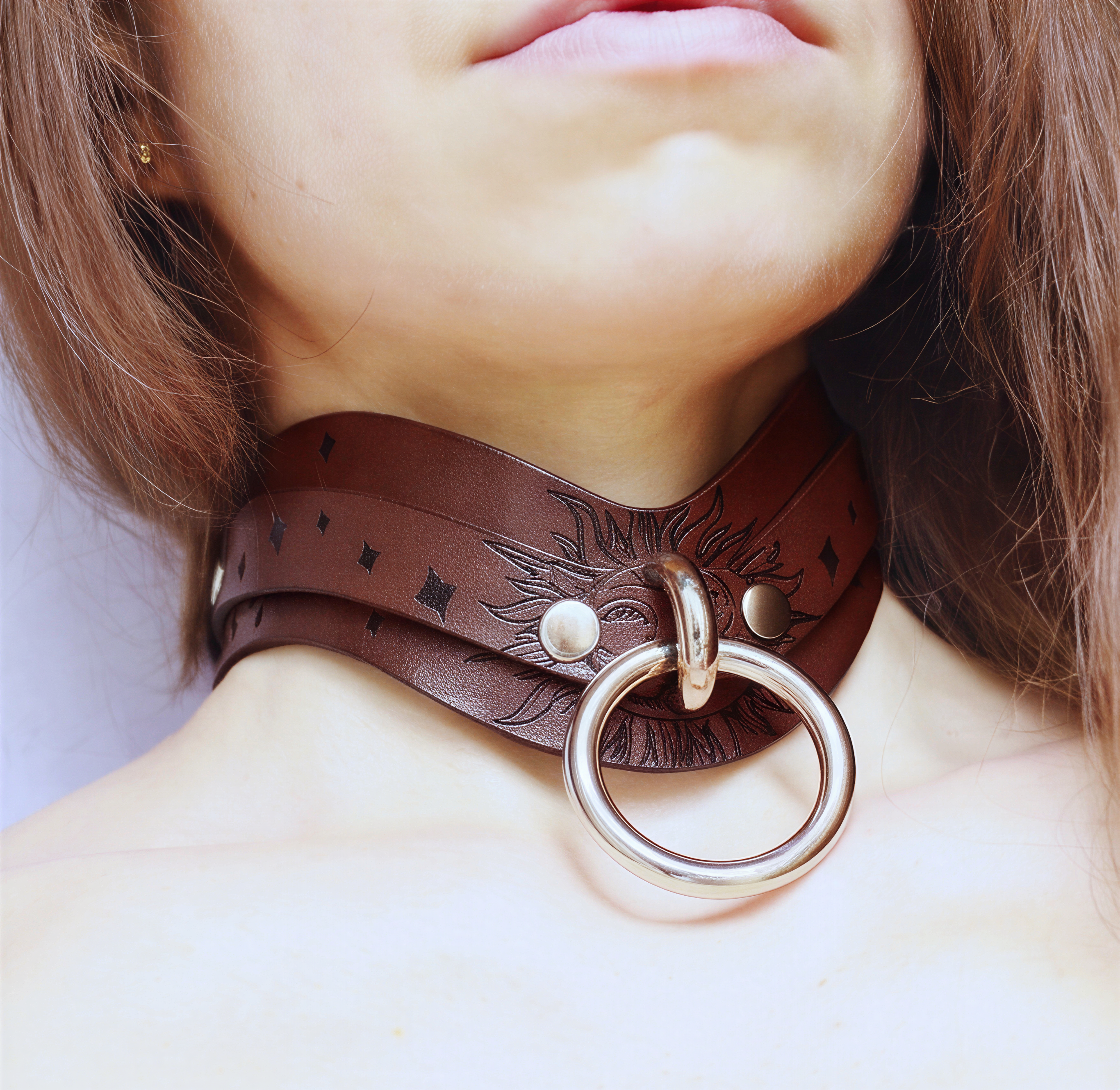 A close-up of a woman's neck and chest area wearing a brown leather choker necklace with a large metal ring.
