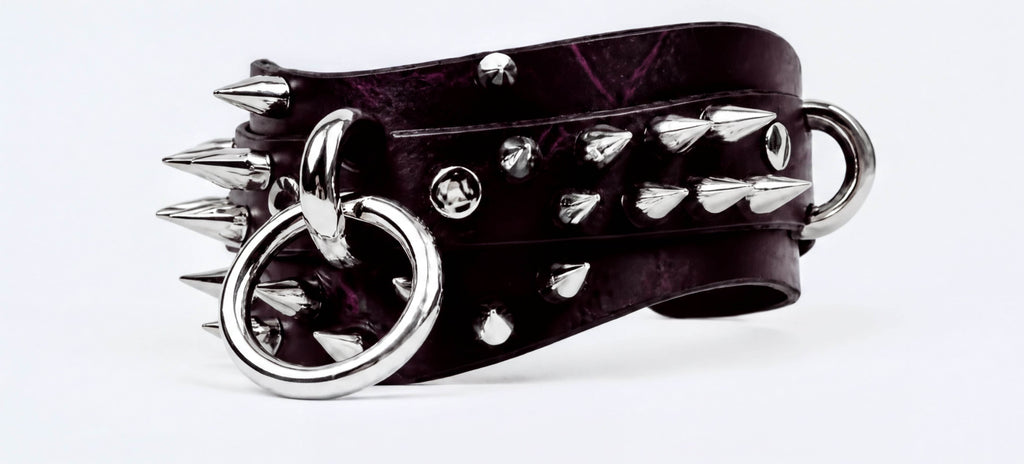 A close-up image of a black leather bracelet with silver spikes and rings, creating a bold and edgy appearance.