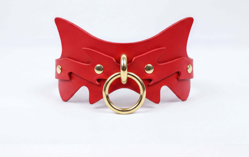 A red leather collar with a gold ring and a unique, cat-like design.