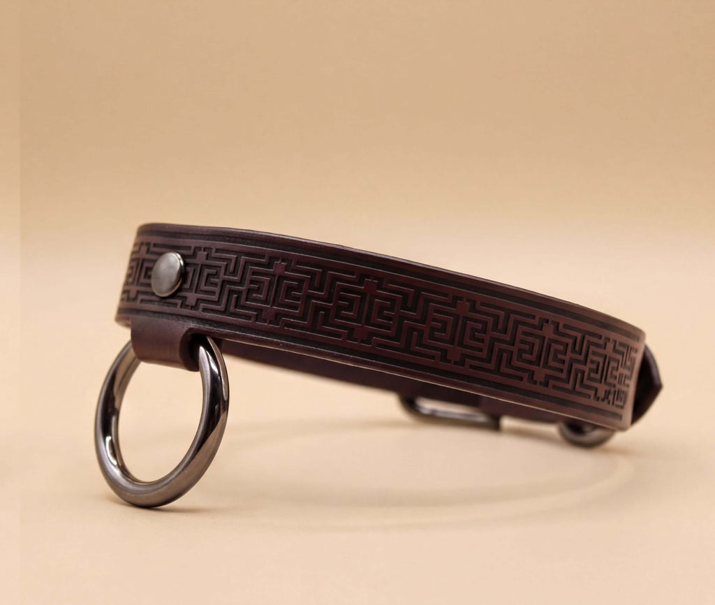 A brown leather collar with a metal ring and a geometric pattern design.