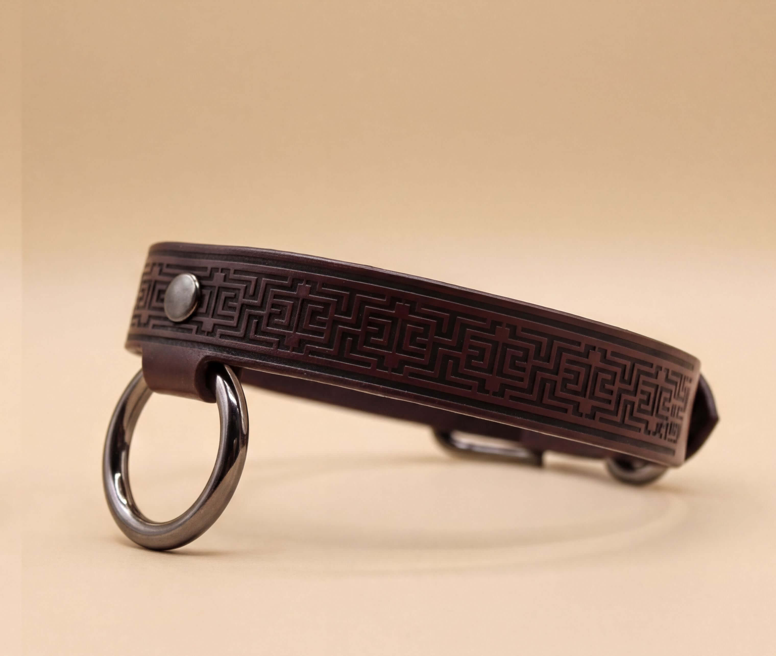 A brown leather collar with a metal ring and a geometric pattern design.