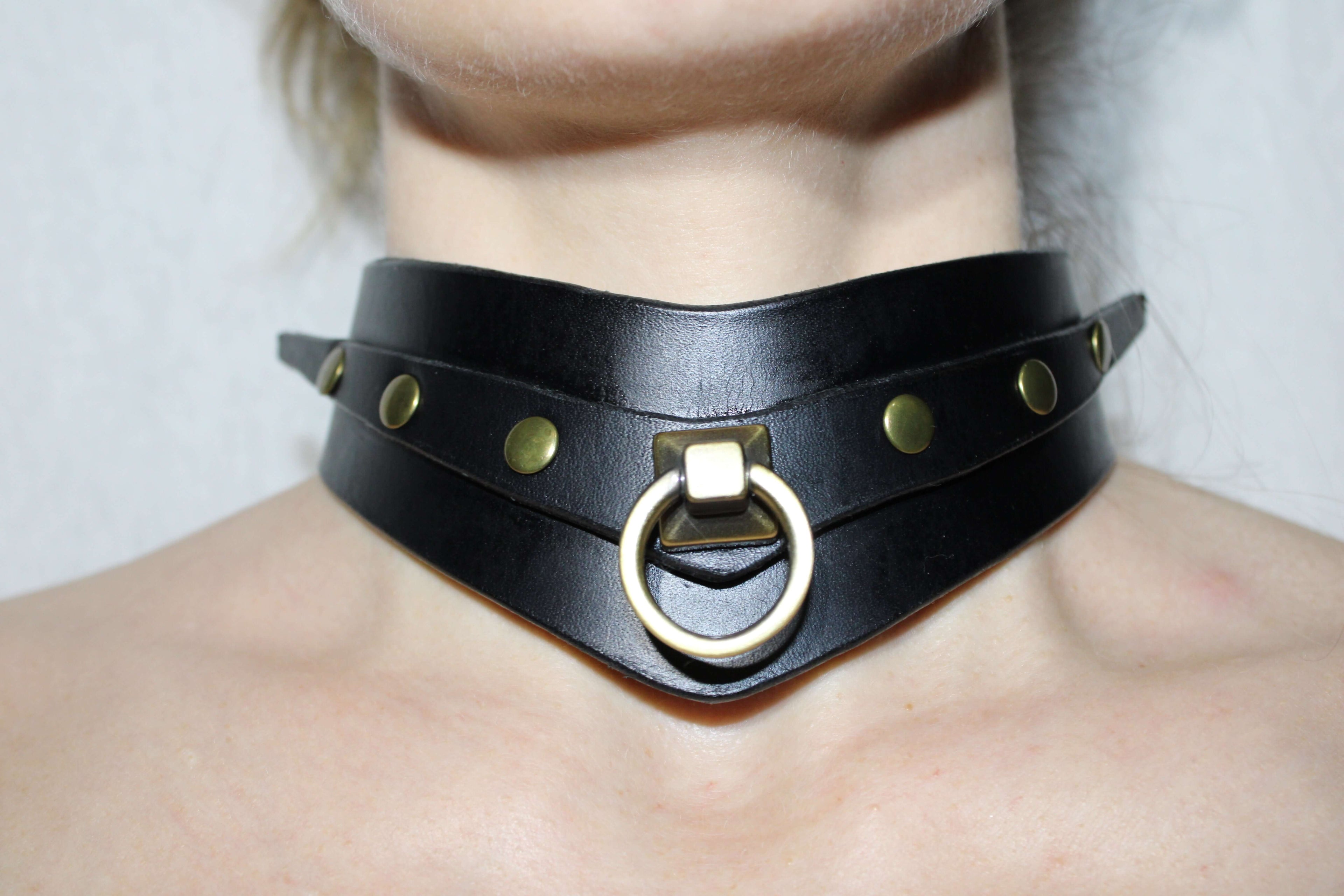 A close-up of a person's neck wearing a black leather choker necklace with a metal ring and studs.