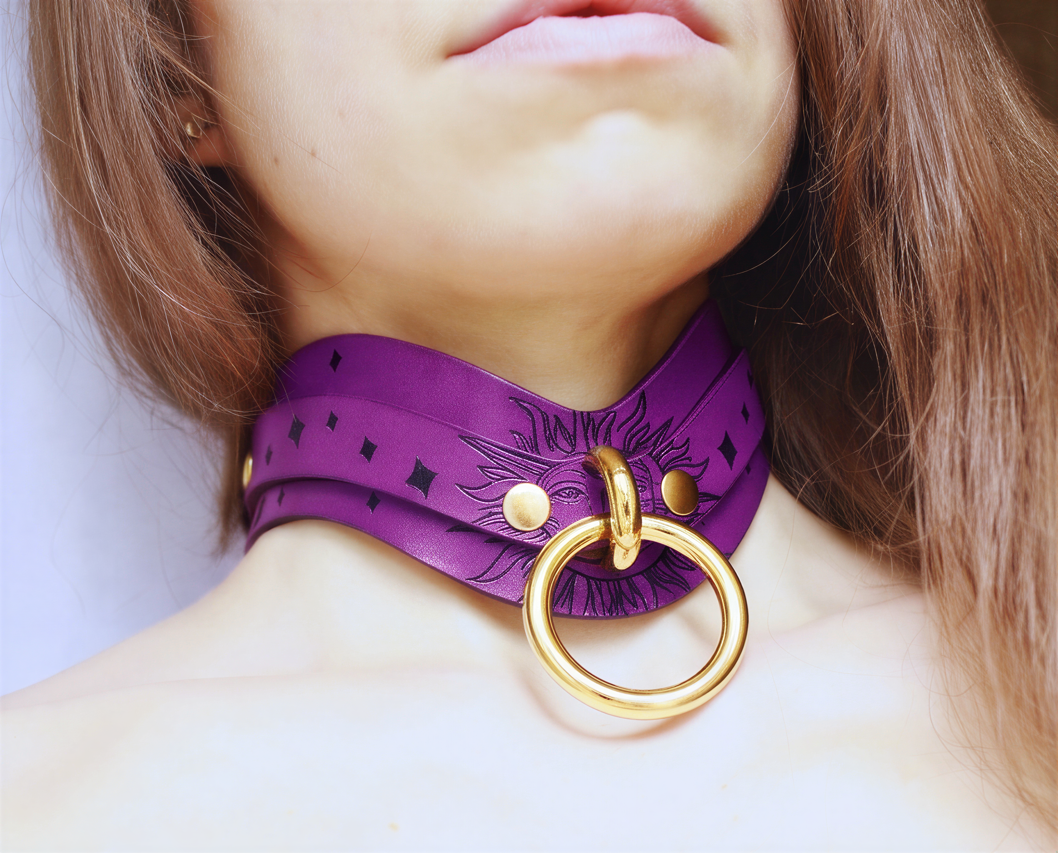 A close-up of a person's neck and chest area wearing a purple choker necklace with a gold ring.