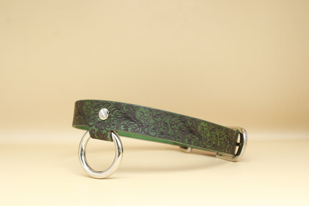 A green leather collar with a metal ring and buckle, set against a beige background.