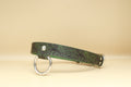 A green leather collar with a metal ring and buckle, set against a beige background.