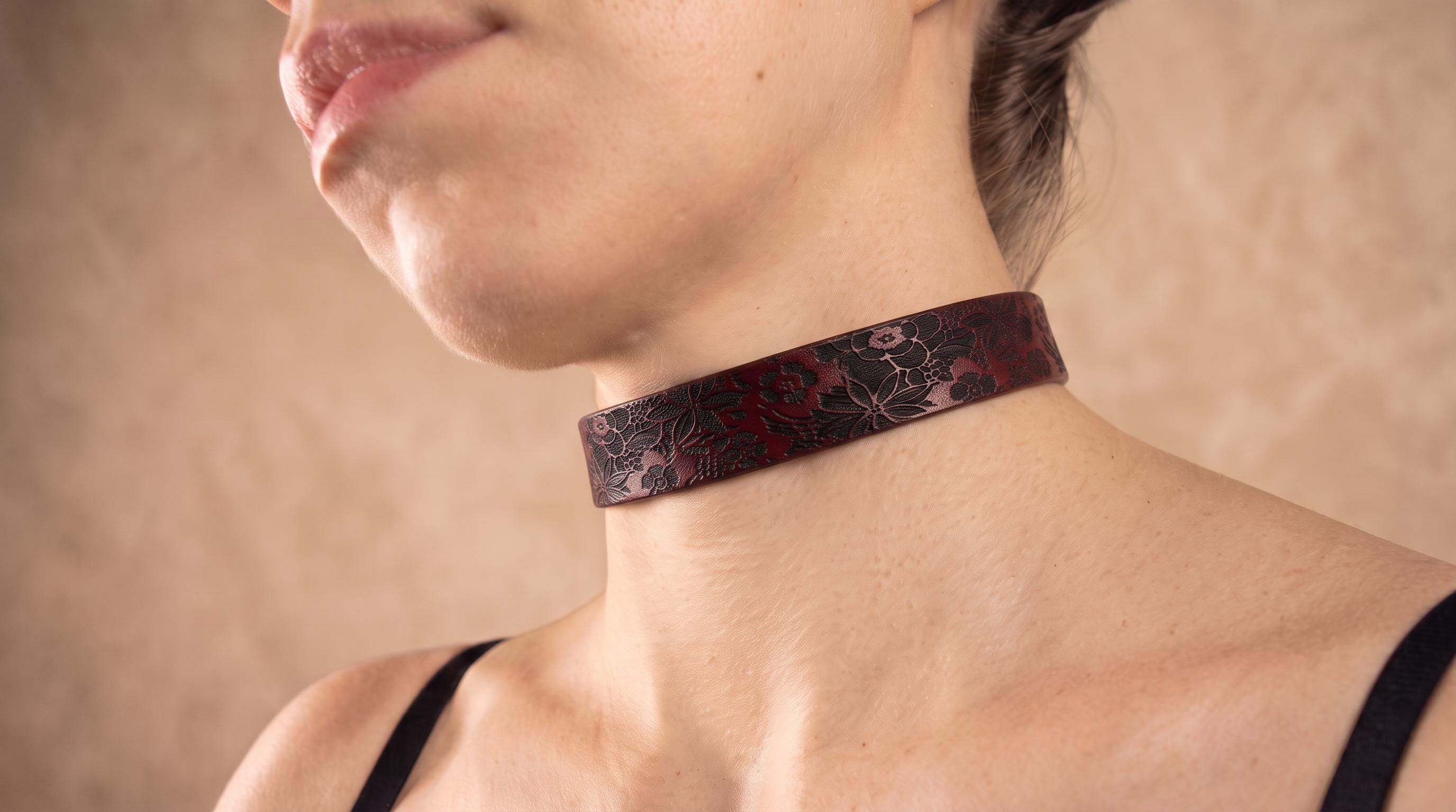 A close-up of a woman's neck and chest area wearing a dark, floral-patterned choker necklace.