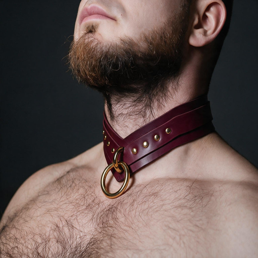 A close-up of a man's neck and chest area, with a burgundy leather choker collar featuring a gold ring and studs.