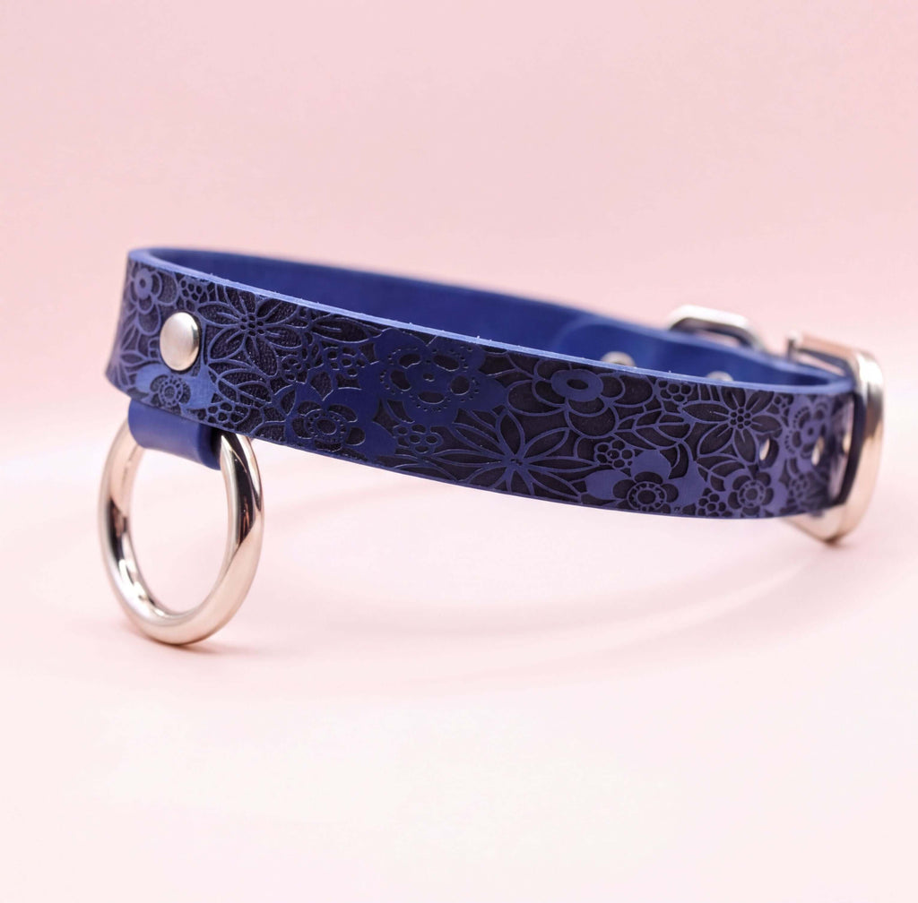 A blue leather collar with a floral pattern and metal rings on the ends.